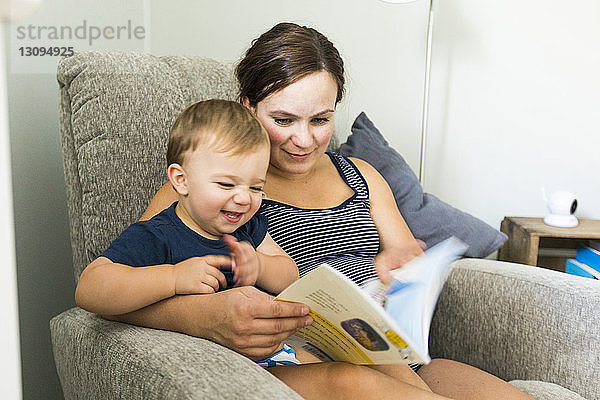 Mutter mit niedlichem Sohn liest Buch  während sie zu Hause auf einem Stuhl sitzt