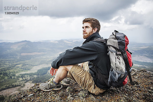 Nachdenklicher Mann mit Rucksack auf Berg sitzend