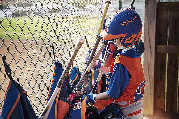 Seitenansicht eines Jungen  der auf dem Spielfeld den Baseballschläger aus der Tasche nimmt