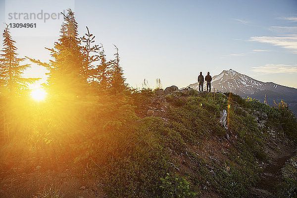 Rückansicht von Wanderern  die bei Sonnenuntergang auf dem Berg gegen den Himmel stehen