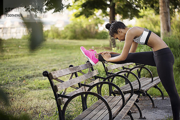Sportliche Frau streckt Bein auf Bank im Park
