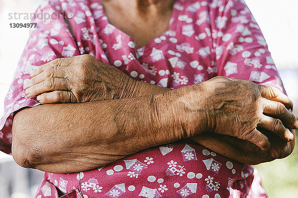 Nahaufnahme einer älteren Frau mit verschränkten Armen im Hinterhof