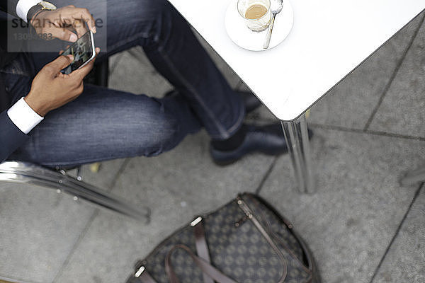 Niedriger Teil eines Geschäftsmannes mit hohem Winkel  der telefoniert  während er im Straßencafé sitzt
