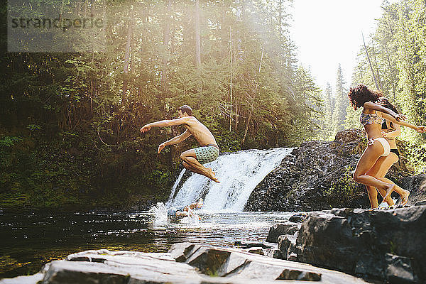 Fröhliche Freunde springen im Wald in den Fluss