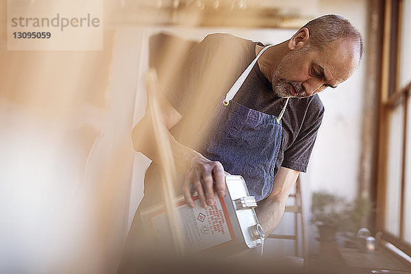 Männlicher Künstler gießt Farbe aus Behälter in Workshop