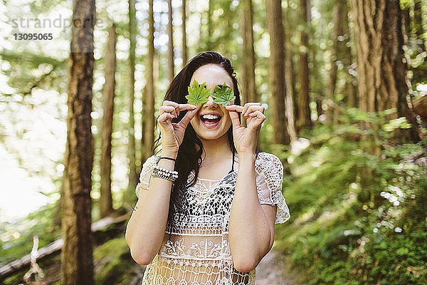 Fröhliche Frau bedeckt Augen mit Blättern im Wald