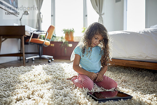 Mädchen benutzt Tablet-Computer  während sie im Schlafzimmer auf dem Teppich kniet