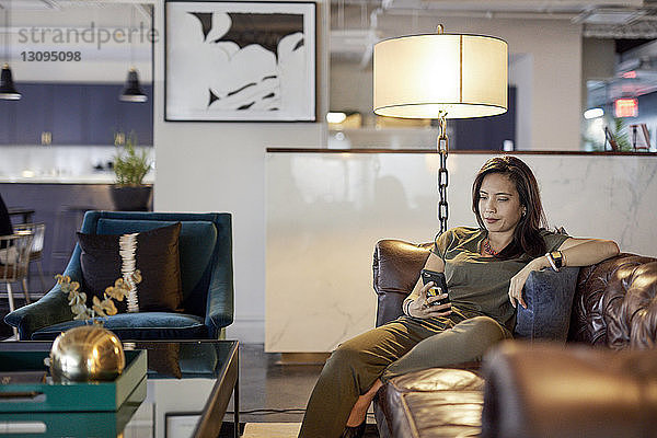 Geschäftsfrau benutzt Smartphone  während sie im Kreativbüro auf dem Sofa sitzt