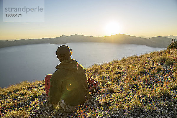 Rückansicht eines Wanderers  der bei Sonnenuntergang auf dem Berg sitzt