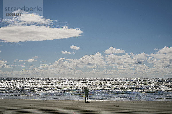Rückansicht einer Wanderin  die am Long Beach vor bewölktem Himmel steht