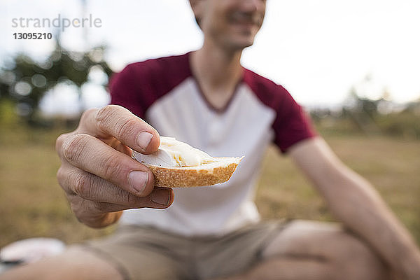 Ein Mann hält Brot in der Mitte  während er auf dem Feld sitzt