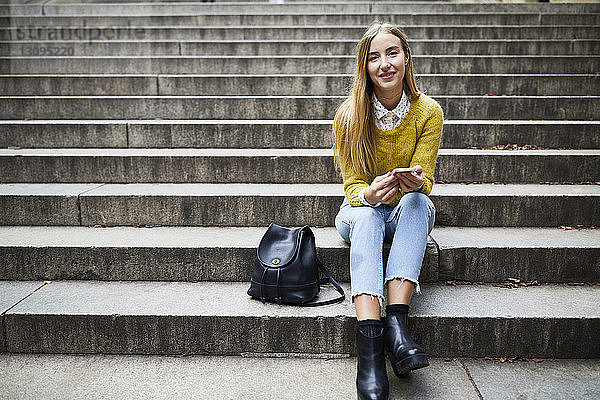 Porträt einer lächelnden jungen Frau  die auf Stufen im Park sitzt