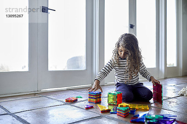 Süßes Mädchen spielt zu Hause auf dem Boden kniend mit bunten Spielzeugklötzen