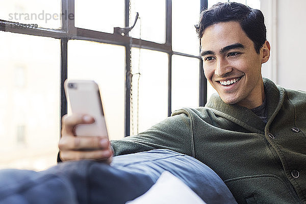 Lächelnder Geschäftsmann am Telefon  während er im Büro auf dem Sofa sitzt