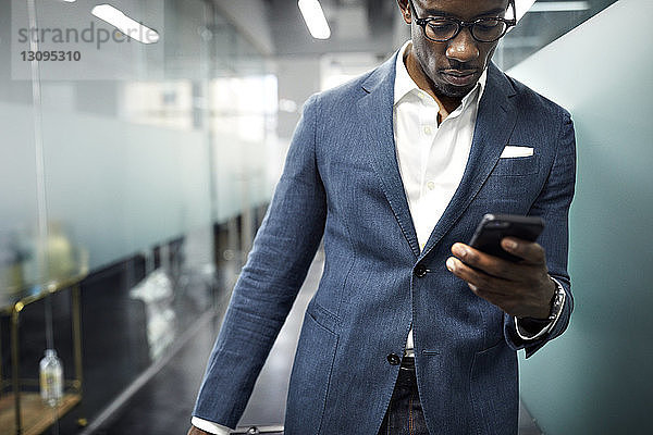 Seriöser Geschäftsmann benutzt Smartphone  während er im Büro steht