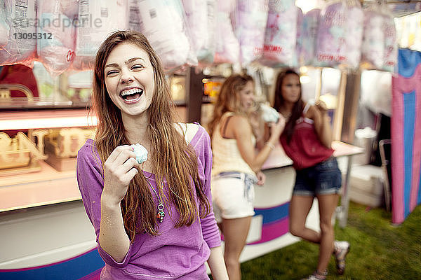 glückliches Teenager-Mädchen hält Zuckerwatte mit Freunden im Hintergrund