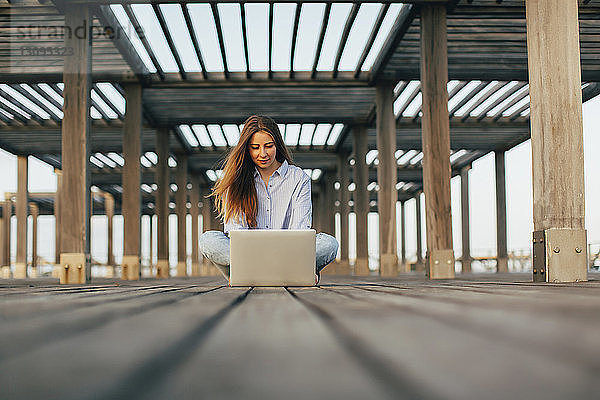 Frau benutzt Laptop-Computer  während sie am Pier sitzt