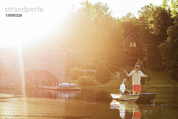Mann wirft Angelschnur im See aus  während ein Freund bei Sonnenschein im Ruderboot sitzt