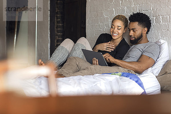 Glückliches multiethnisches Paar benutzt Tablet-Computer am Bett