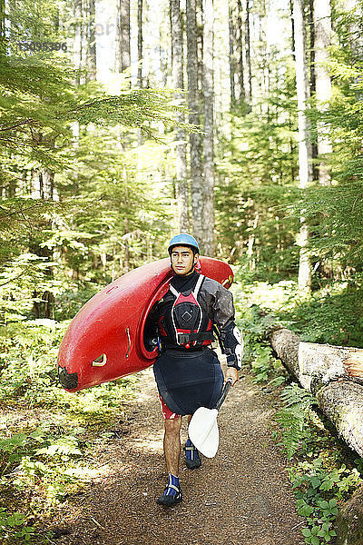 Junger Mann trägt Kajak beim Waldspaziergang