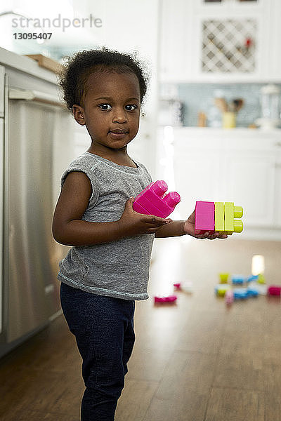 Porträt eines Mädchens  das Spielzeugblöcke hält  während es zu Hause in der Küche steht