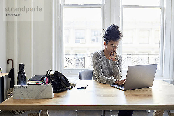 Seriöse Geschäftsfrau benutzt Laptop-Computer am Schreibtisch gegen Fenster im Büro