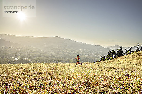 Seitenansicht einer Frau  die während eines sonnigen Tages auf einem Grasfeld gegen den Himmel joggt