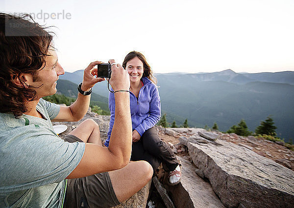 Frau betrachtet Freund beim Fotografieren  während sie auf Berg sitzt