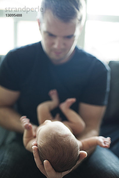 Vater hält neugeborenen Jungen  während er zu Hause sitzt