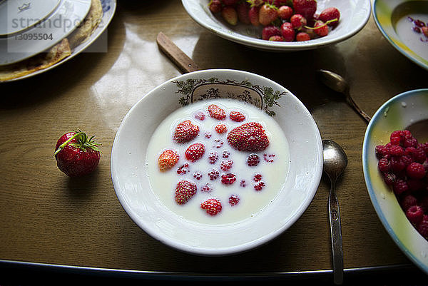 Hochwinkelansicht von Erdbeeren und Milch in Schale auf Holztisch