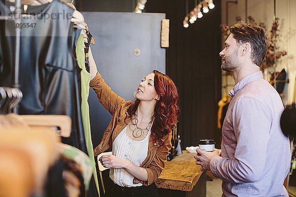 Lächelnder Besitzer zeigt Kleidungsstücke einem männlichen Kunden im Laden