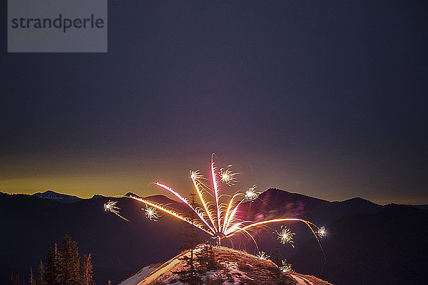 Feuerwerk auf dem Hügel vor der Silhouette der Bergkette bei Sonnenuntergang