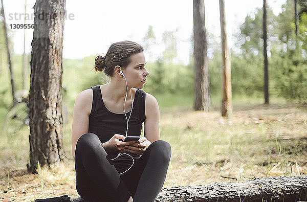 Frau hört Musik  während sie auf einem Feld im Wald sitzt