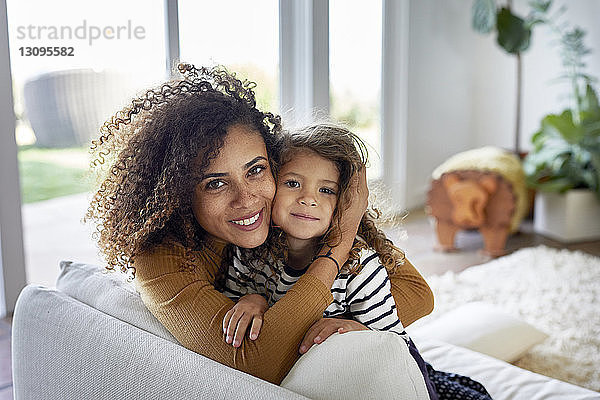 Porträt einer Mutter  die ihre Tochter umarmt  während sie zu Hause auf dem Sofa sitzt