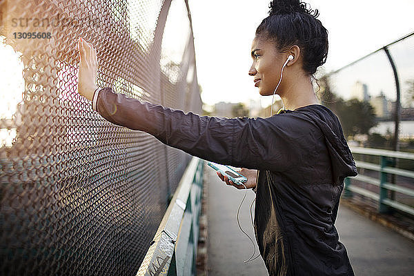 Seitenansicht einer sportlichen Frau  die Musik hört  während sie am Zaun steht
