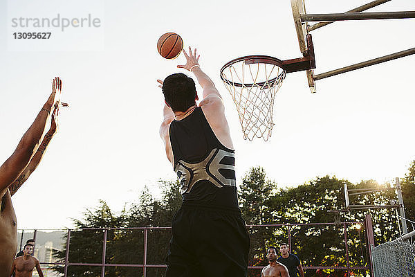 Mann spielt mit Freunden vor Gericht gegen klaren Himmel Basketball