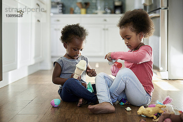 Schwestern spielen mit Eisspielzeug  während sie zu Hause auf dem Hartholzboden sitzen