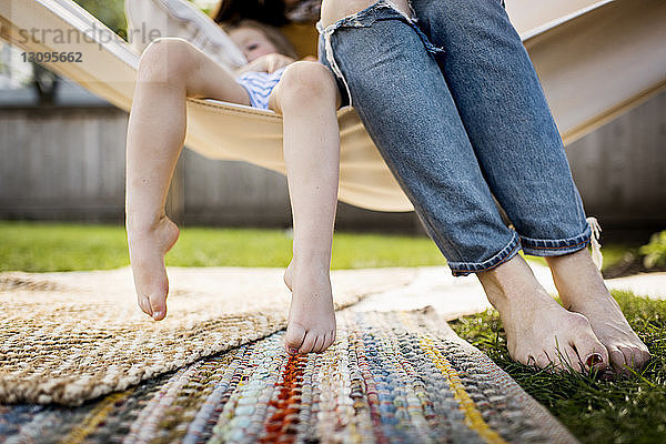 Unterer Teil der Mutter mit Tochter in Hängematte im Hof sitzend