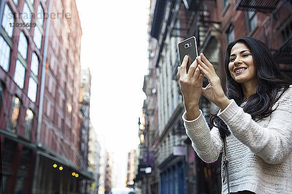 Glückliche junge Frau fotografiert durch Smartphone in der Stadt