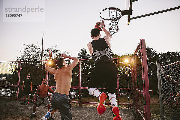 Männliche Freunde spielen bei Sonnenuntergang Basketball auf dem Platz