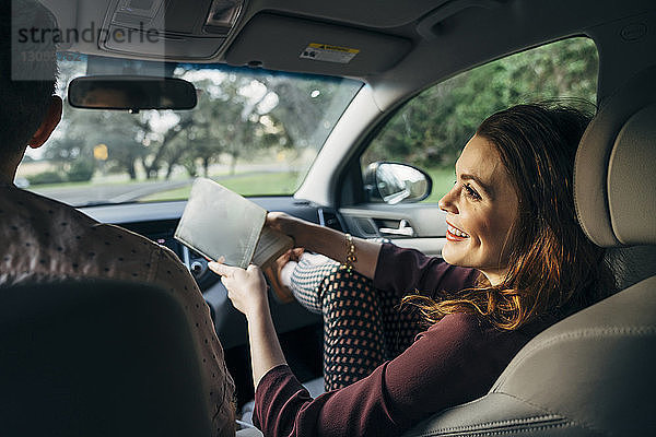 Lächelnde Frau hält Buch  während sie im Auto mit dem Ehemann spricht