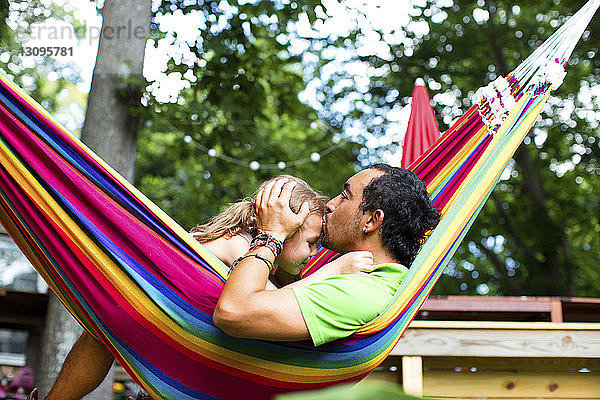 Mann küsst Tochter auf die Stirn  während er sich in Hängematte im Hinterhof entspannt