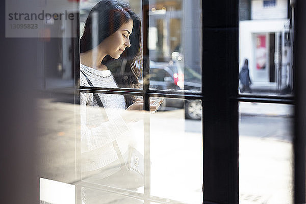 Junge Frau mit Smartphone durch Glaswand gesehen