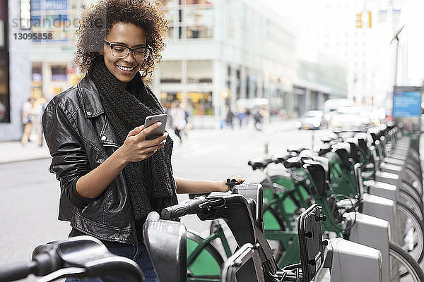 Glückliche Frau benutzt Mobiltelefon  während sie am Fahrradträger steht
