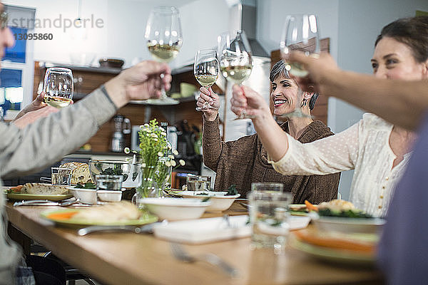 Glückliche Freunde stoßen bei geselligem Beisammensein am Tisch auf Wein an