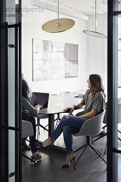 Weibliche Kollegen diskutieren über Laptop-Computer im Konferenzraum mit Blick durch die Tür