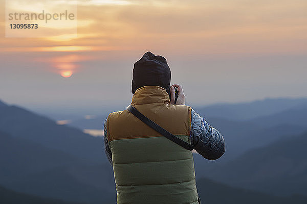 Rückansicht eines männlichen Wanderers  der bei Sonnenuntergang Berge fotografiert