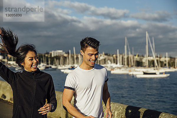 Glückliches junges Paar beim Joggen auf der Promenade bei bewölktem Himmel in der Stadt