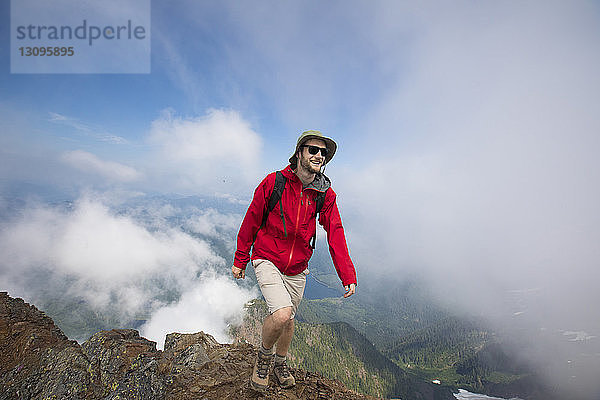 Glücklicher Wanderer steht auf Berg gegen wolkigen Himmel