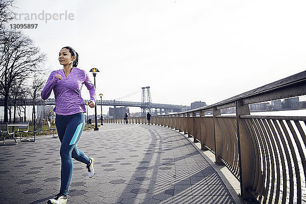 Entschlossene Athletin läuft auf einem Fußweg mit der Williamsburg Bridge im Hintergrund